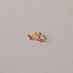 Introducing Butterfly Birthstone Flatback Studs—small gold butterfly earrings with pink gemstones, displayed on a light grey surface for a personalized jewelry touch to any look.