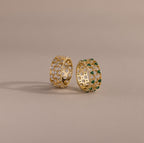 Two checkered band rings, one with diamonds and one with emeralds, each round-cut CZ stones set in an openwork grid design, displayed on a neutral background.