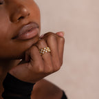 Close-up of model wearing a gold checkered diamond ring, featuring a wide band with open grid design and sparkling round-cut stones.