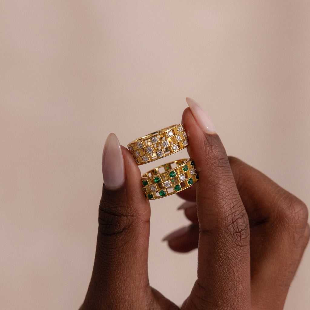 Model holding two checkered band rings, one with diamonds and one with emeralds, each round-cut CZ stones set in an openwork grid design.