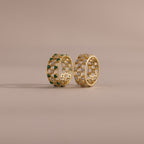 Two checkered band rings, one with diamonds and one with emeralds, each round-cut CZ stones set in an openwork grid design, displayed on a neutral background.