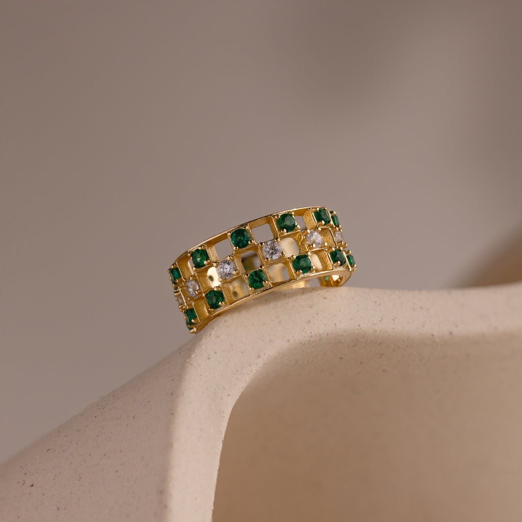 Gold checkered band ring featuring alternating rows of emerald and diamond round-cut CZ stones set in an openwork grid design.