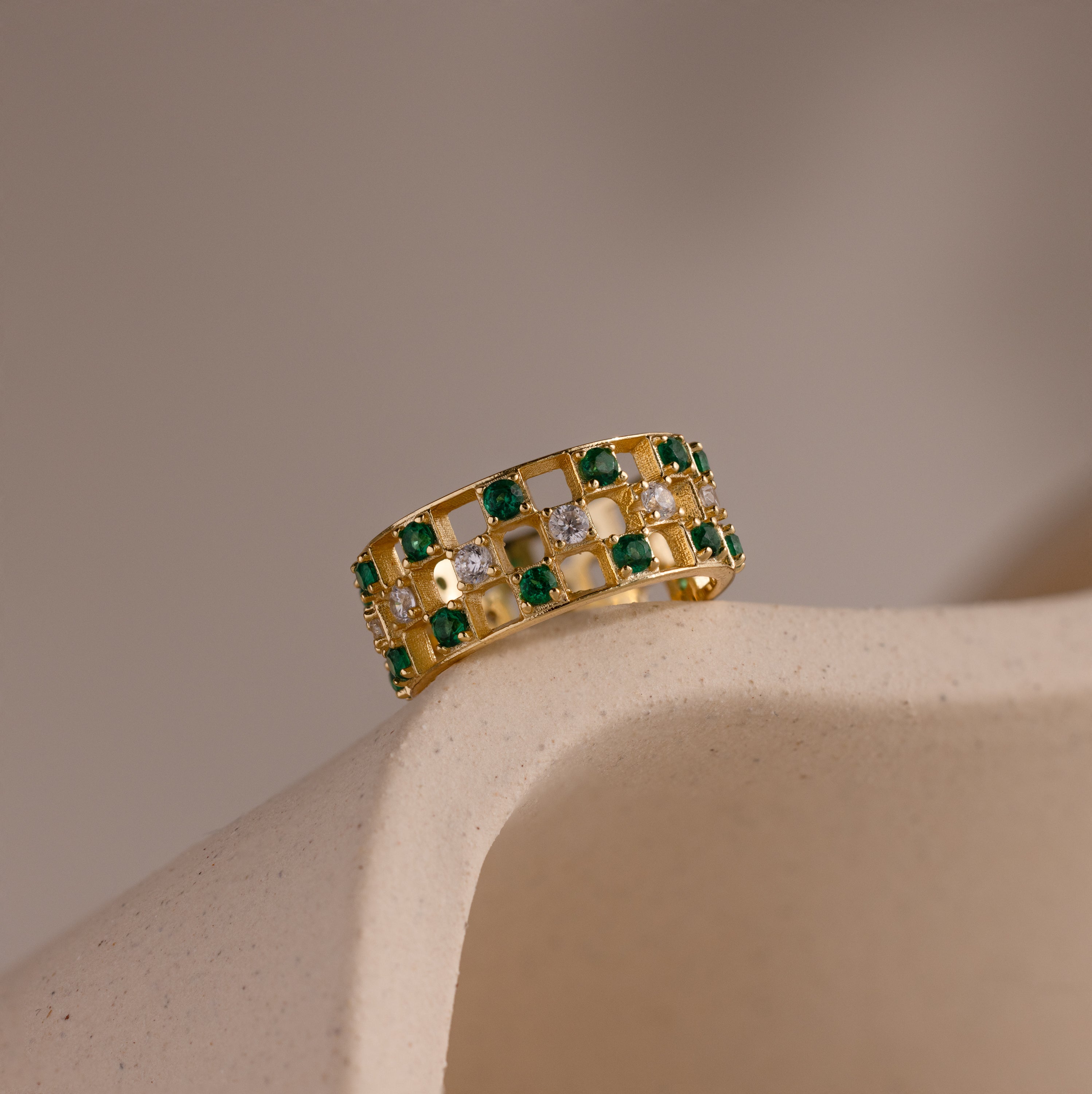 Gold checkered band ring featuring alternating rows of emerald and diamond round-cut CZ stones set in an openwork grid design.