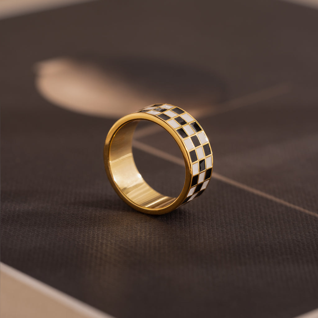 Side-view of a gold ring with a thick band featuring a black and white enamel checkerboard pattern.