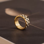 Side-view of a gold ring with a thick band featuring a black and white enamel checkerboard pattern.