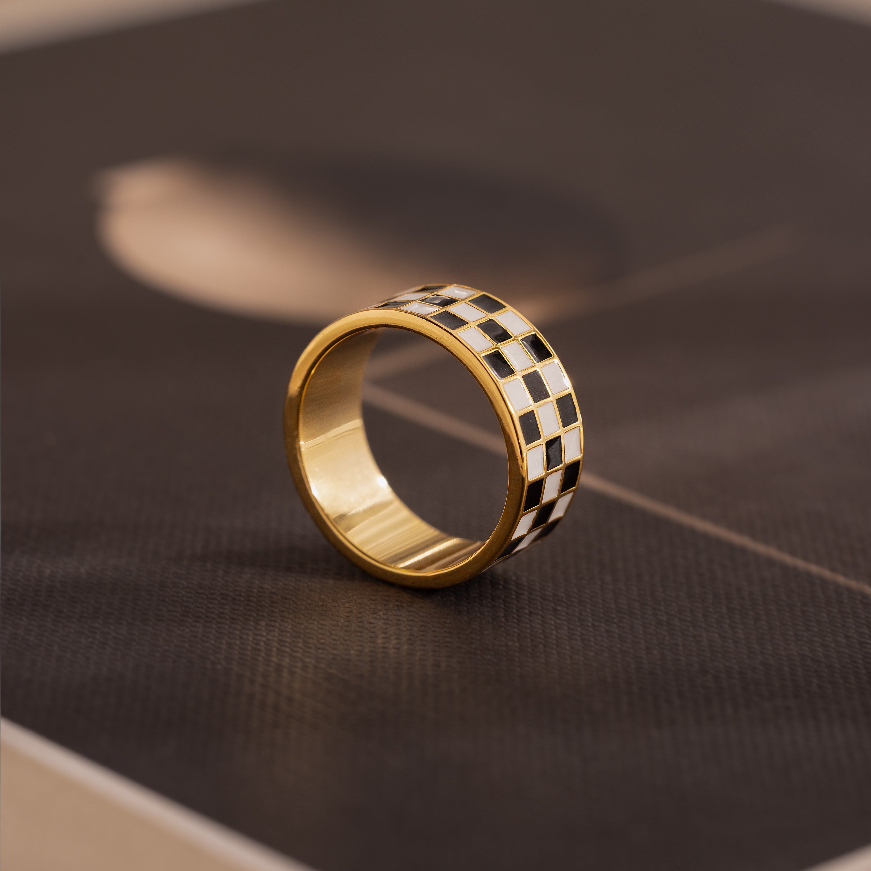 Side-view of a gold ring with a thick band featuring a black and white enamel checkerboard pattern.