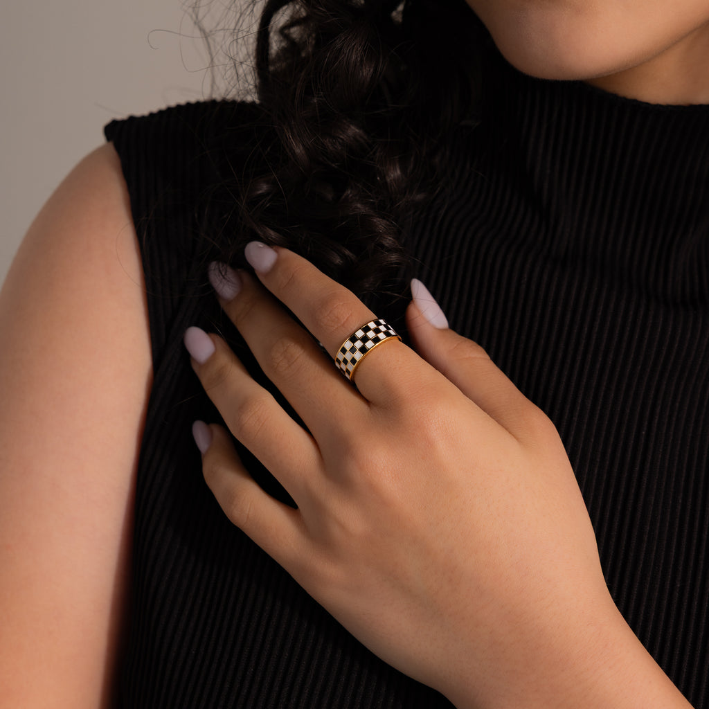 Model wearing a gold ring with a thick band featuring a black and white enamel checkerboard pattern.