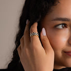 Model wearing a gold ring with a thick band featuring a black and white enamel checkerboard pattern.