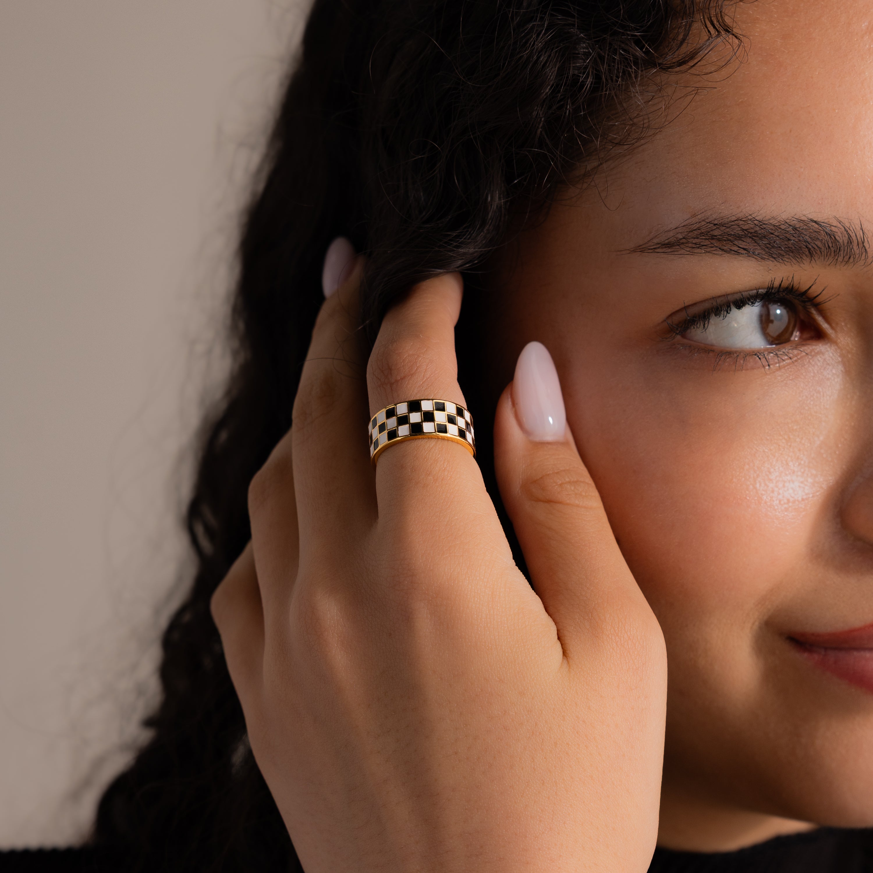 Model wearing a gold ring with a thick band featuring a black and white enamel checkerboard pattern.