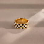 Gold ring with a thick band featuring a black and white enamel checkerboard pattern.