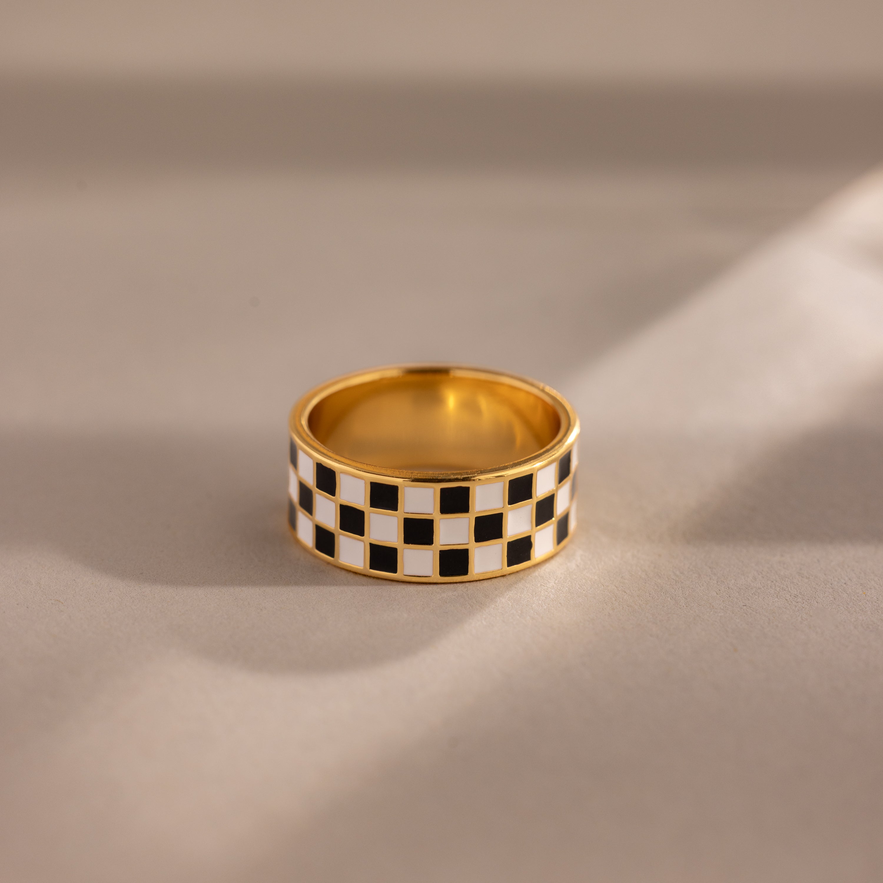 Gold ring with a thick band featuring a black and white enamel checkerboard pattern.
