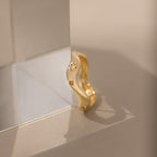 The Wavy Diamond Celestial Ring features small star-shaped engravings and is pictured resting against a clear glass block on a beige surface.