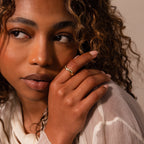 A woman with curly hair gazes to the side, her hand near her face, showcasing the Wavy Diamond Celestial Ring.