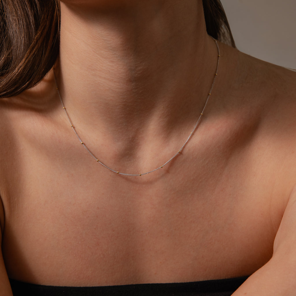 A woman in a black strapless top showcases her neck and collarbone, wearing a delicate satellite chain necklace—ideal for layering or pairing with the Mixed Metal Beaded Necklace.