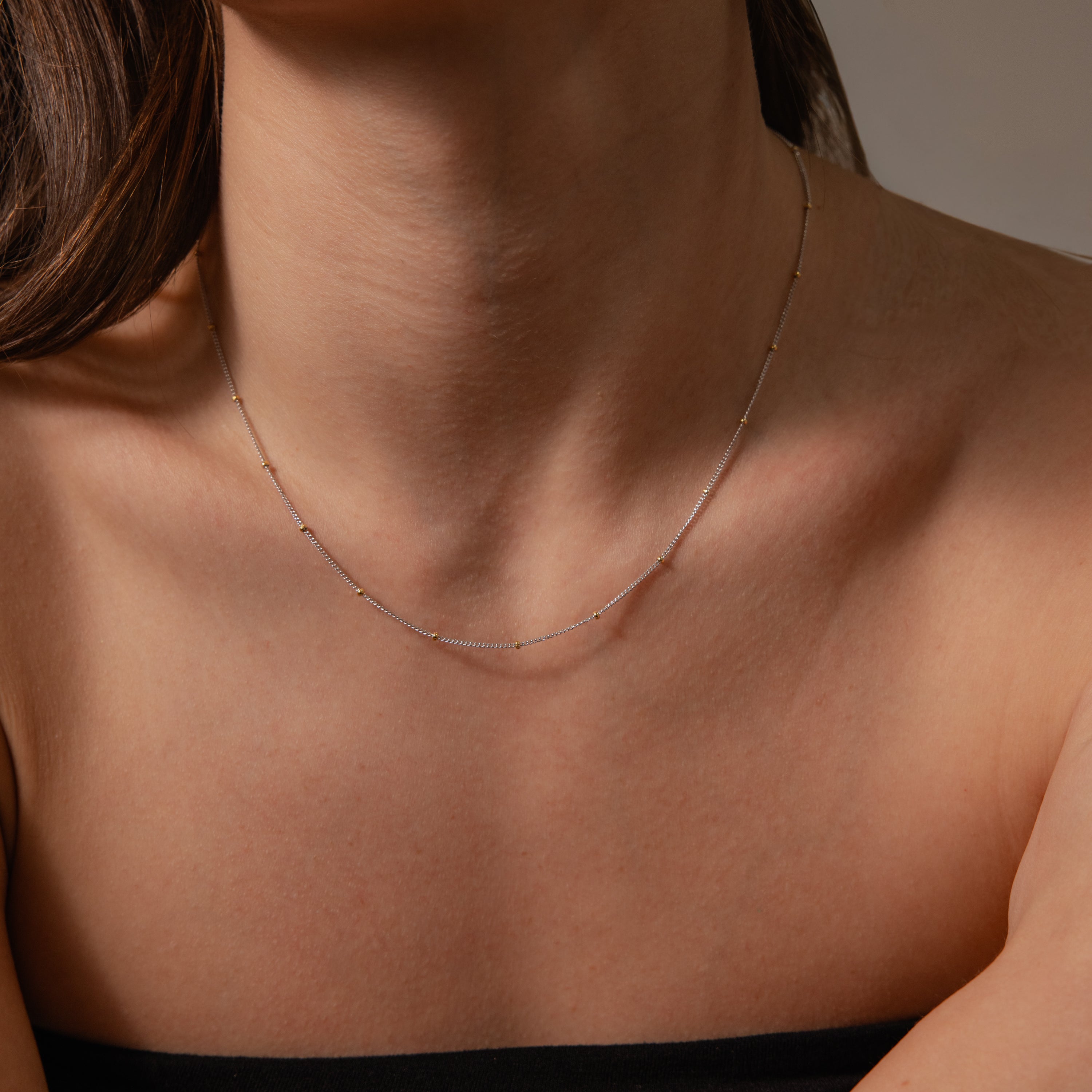 A woman in a black strapless top showcases her neck and collarbone, wearing a delicate satellite chain necklace—ideal for layering or pairing with the Mixed Metal Beaded Necklace.