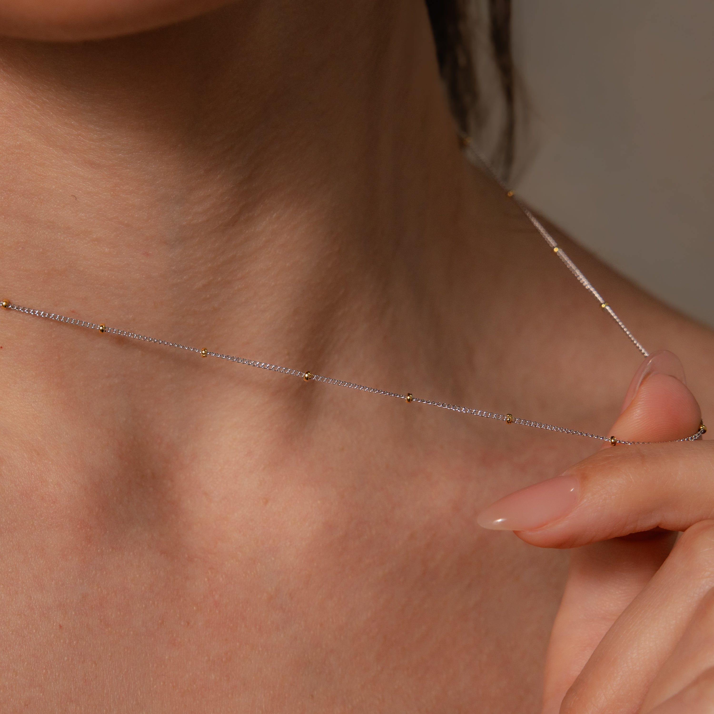 A close-up of a woman’s neck and hand showcasing the Mixed Metal Beaded Necklace featuring small gold beads, perfect for layering.