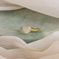 The Moonstone Heart Ring features a radiant heart-shaped stone, displayed on green marble and accented by soft cream fabric.