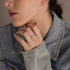 A woman wearing a denim jacket showcases the Moonstone Heart Ring, its luminous heart-shaped stone reflecting light as she rests her hand near her chin.