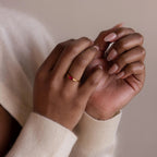 Hands with nude nails wearing the Marquise Birthstone Signet Ring, featuring a red marquise-cut gemstone, paired with a cream sweater against a neutral background.