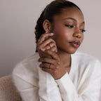 A woman in a white sweater poses with hands near her face, thoughtfully displaying the Marquise Birthstone Signet Ring along with other statement rings.