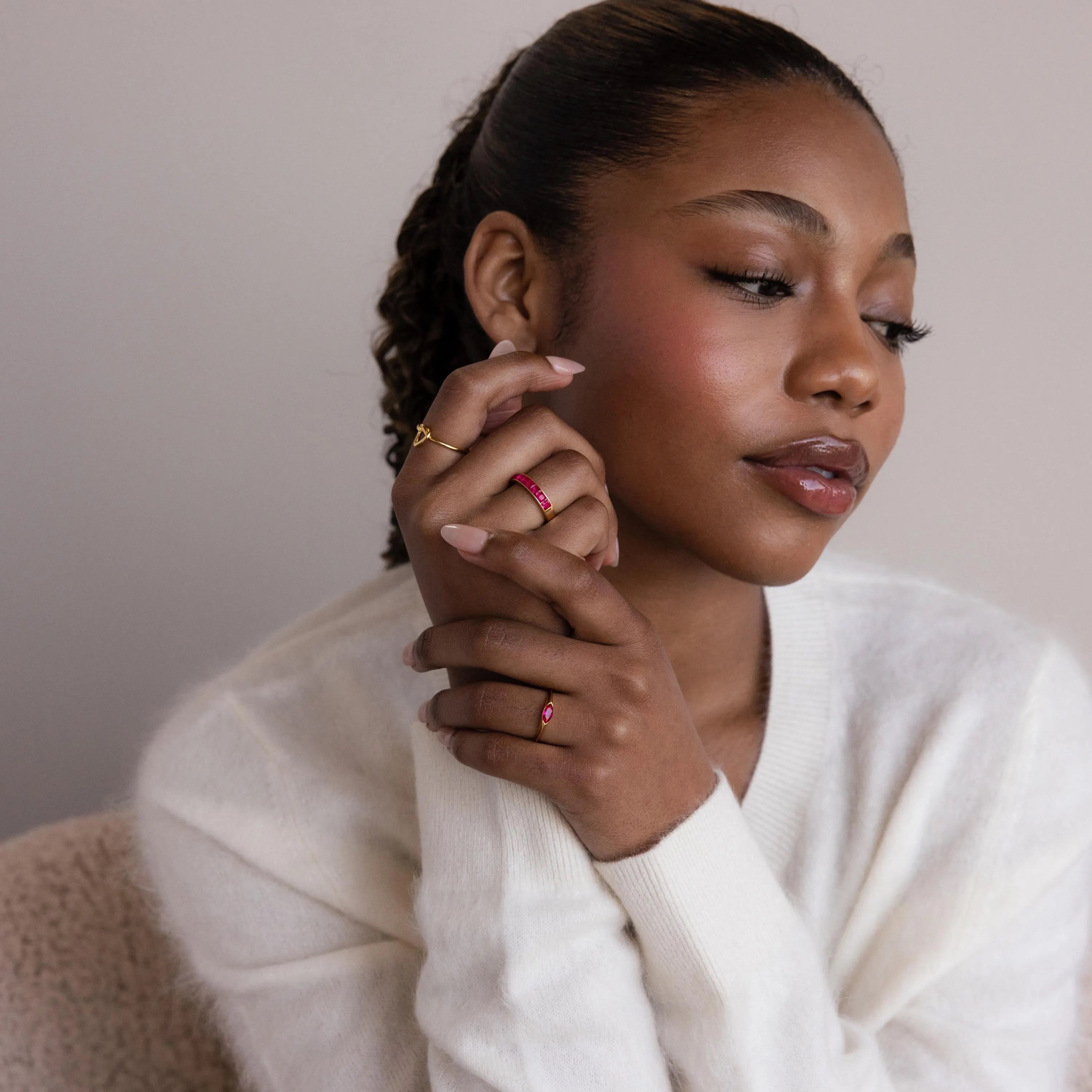 A woman in a white sweater poses with hands near her face, thoughtfully displaying the Marquise Birthstone Signet Ring along with other statement rings.