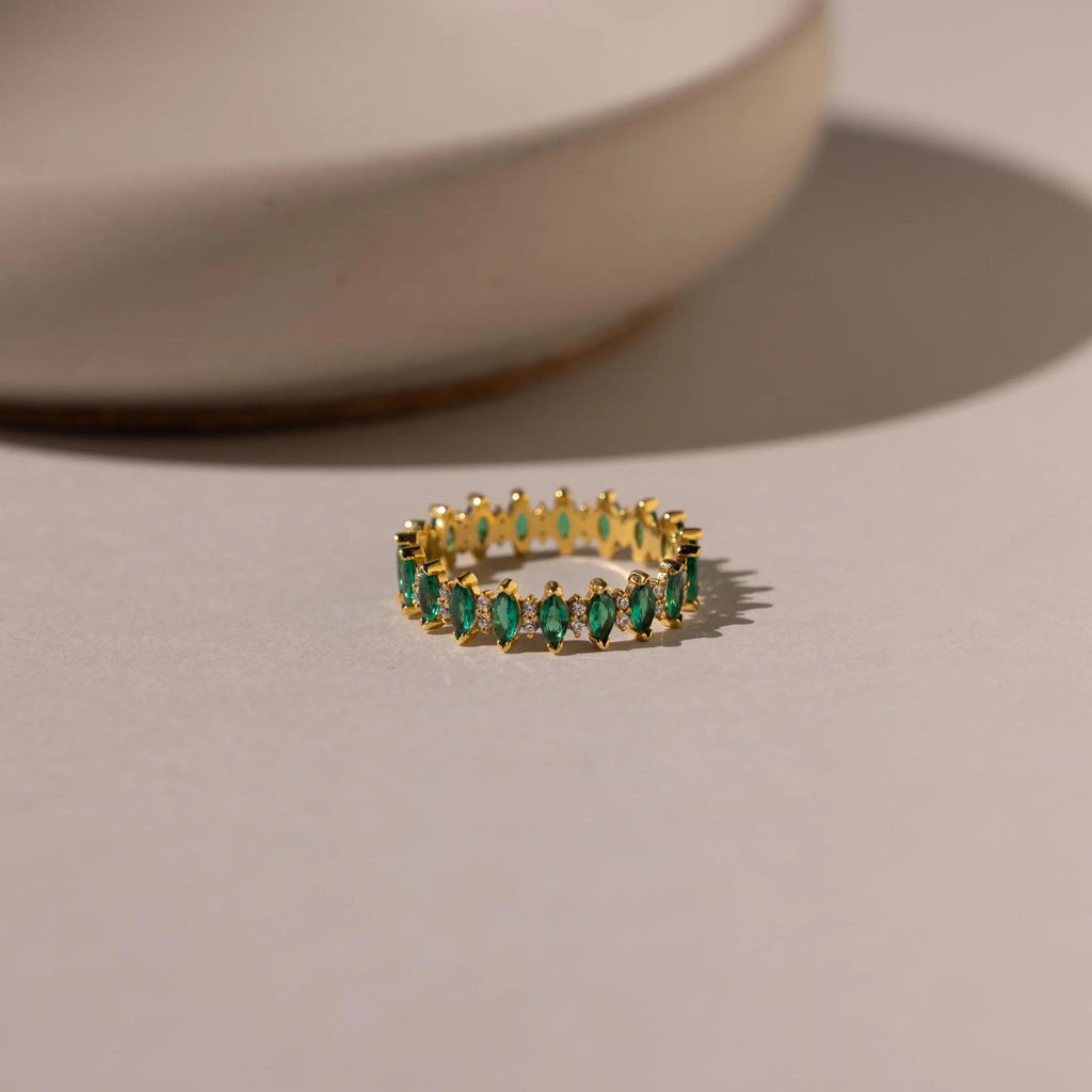 Marquise Infinity Birthstone Ring with green marquise stones encircling the band, shown on a light surface against a blurred background.