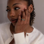 A woman in a white sweater touches her face while wearing the Marquise Infinity Birthstone Ring, featuring blue stones on her hand.