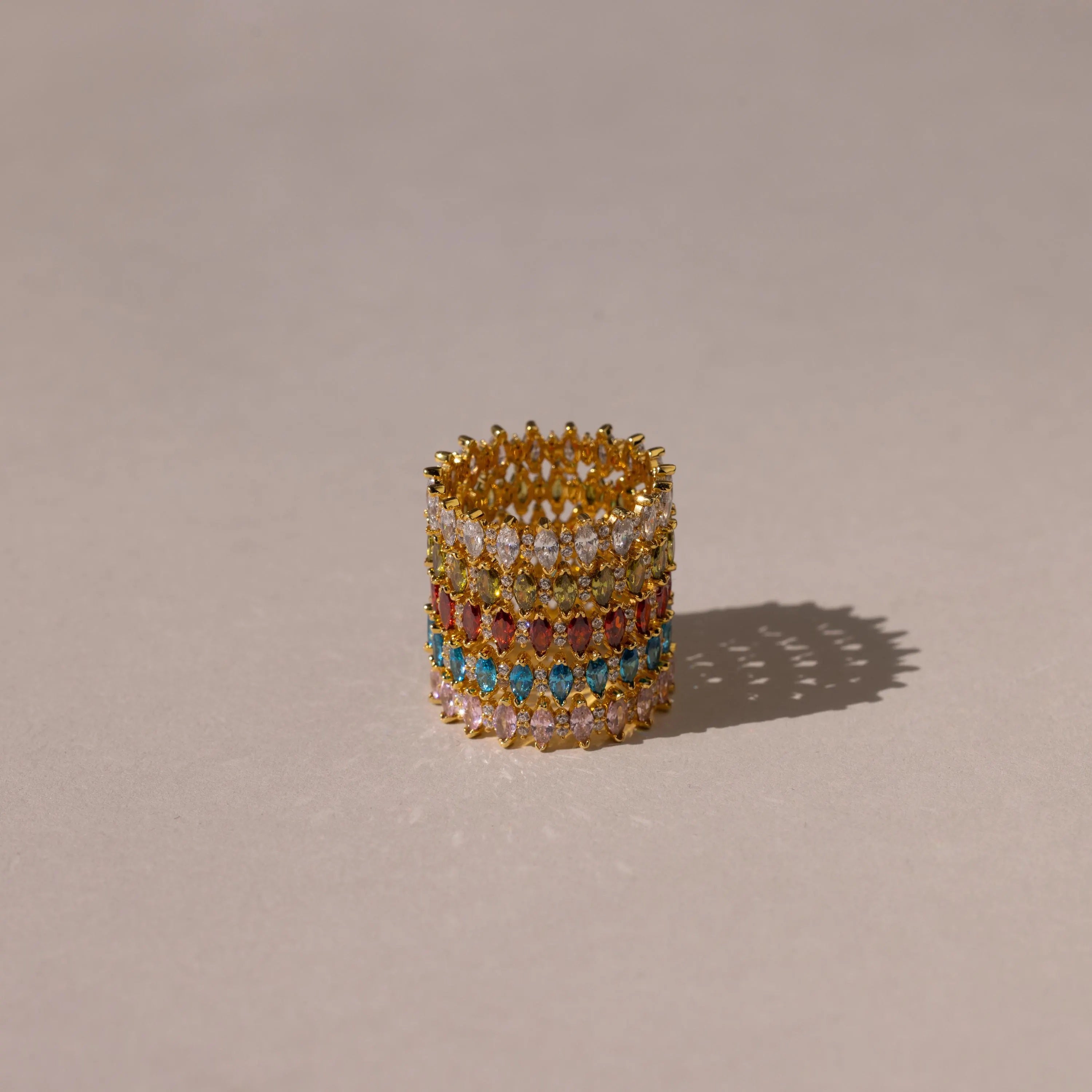 The Marquise Infinity Birthstone Ring, with vibrant gemstones arranged in multiple rows, rests on a neutral background and casts a gentle shadow.