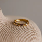 A gold band ring and an 18K gold tennis ring with purple gemstones, placed on a neutral surface.