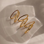 A gradient lineup of four gold birthstone bands with amethyst, onyx, sapphire, and diamond-like stones, casting elegant shadows on soft beige fabric.