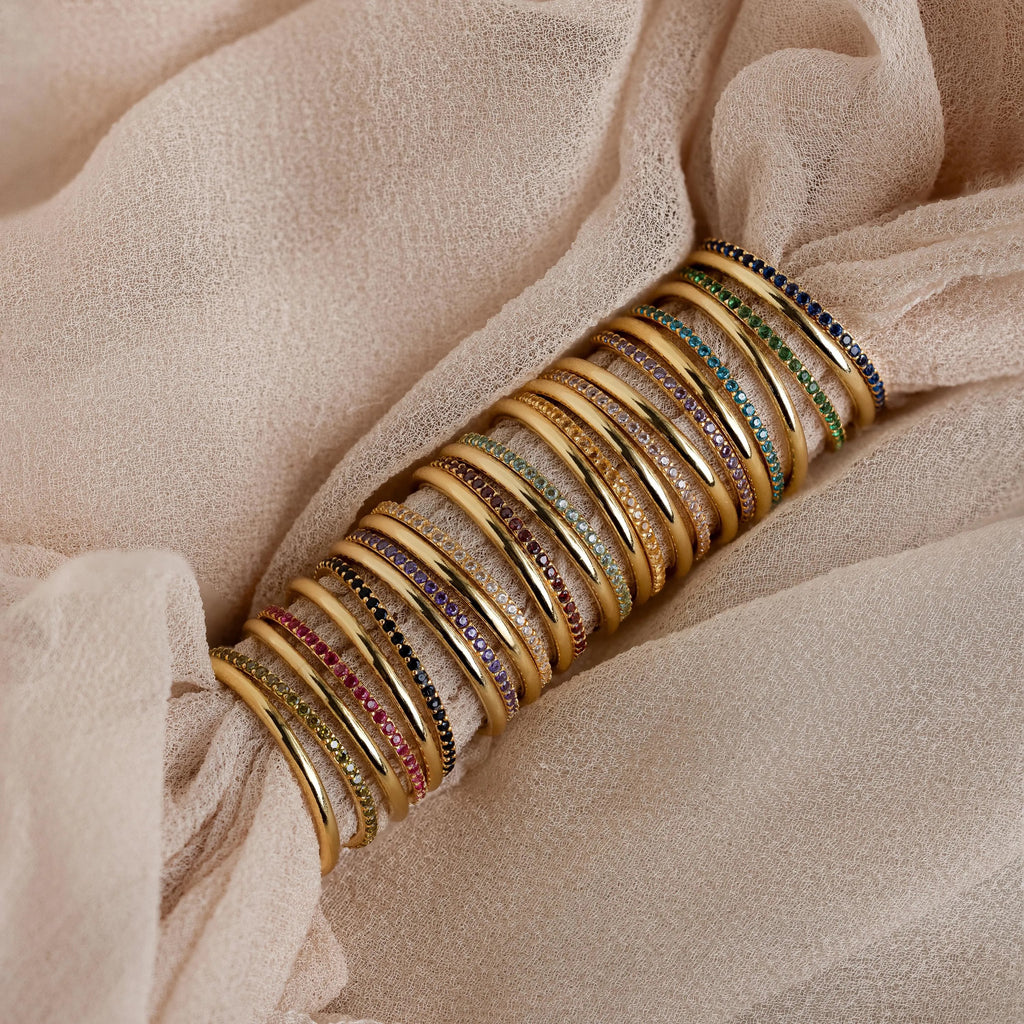 A striking full set of birthstone rings in gold finish, showcasing stones in every month’s color from garnet to zircon, wrapped over soft champagne-colored fabric.