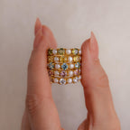 A hand displays four stacked Birthstone Pearl Lace Rings, each adorned with pearls, vibrant gemstones, and a sparkling birthstone accent.