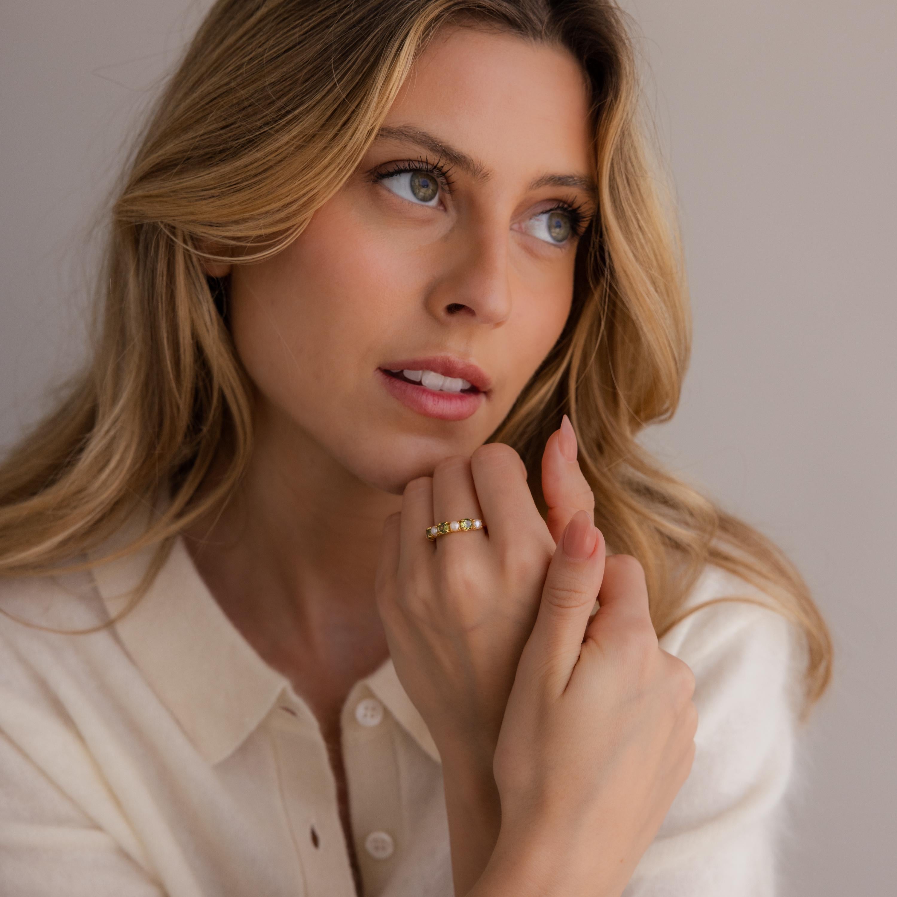A woman with wavy blonde hair, wearing a cream top and the Birthstone & Pearl Lace Ring, gazes thoughtfully to the side.