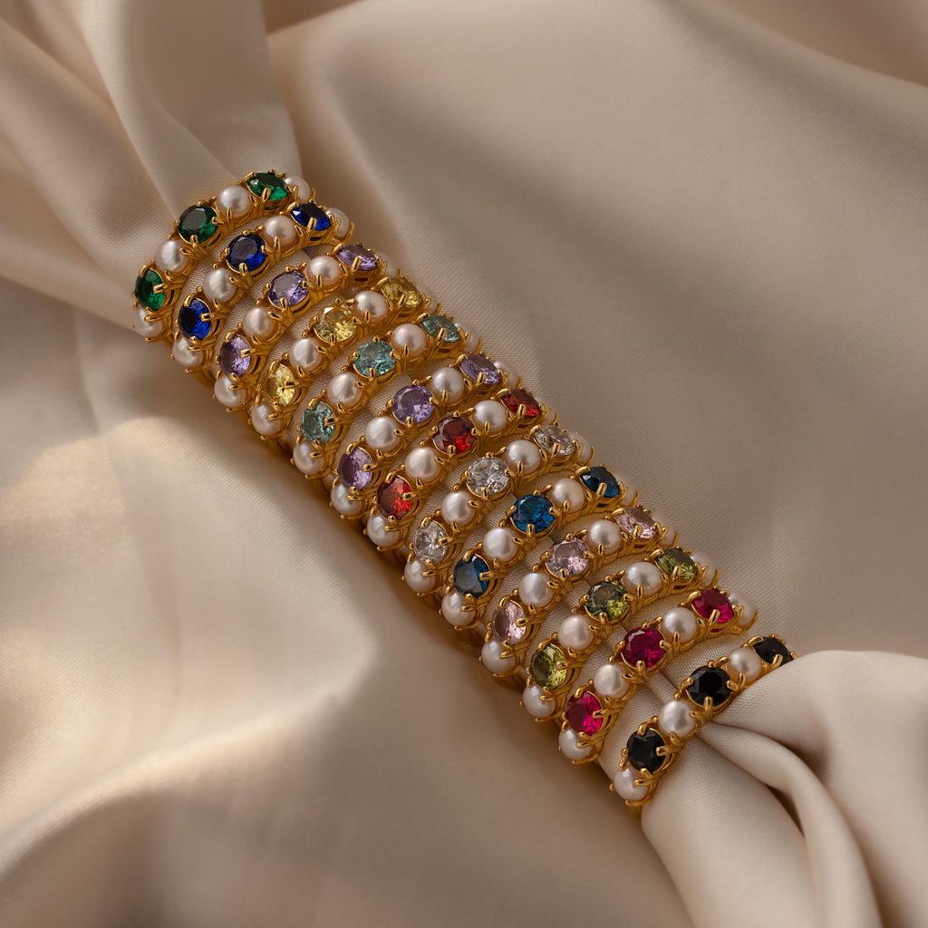 The Birthstone & Pearl Lace Ring features vibrant stones and pearls on white lace, accented with a delicate gold band for an elegant touch.