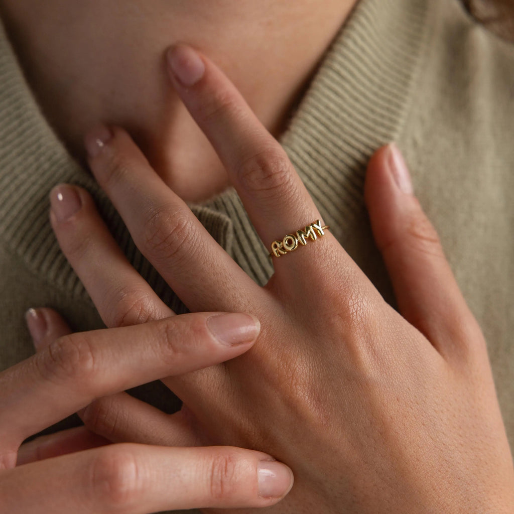 Model wearing a dainty gold bubble letter ring with the name "ROMY".