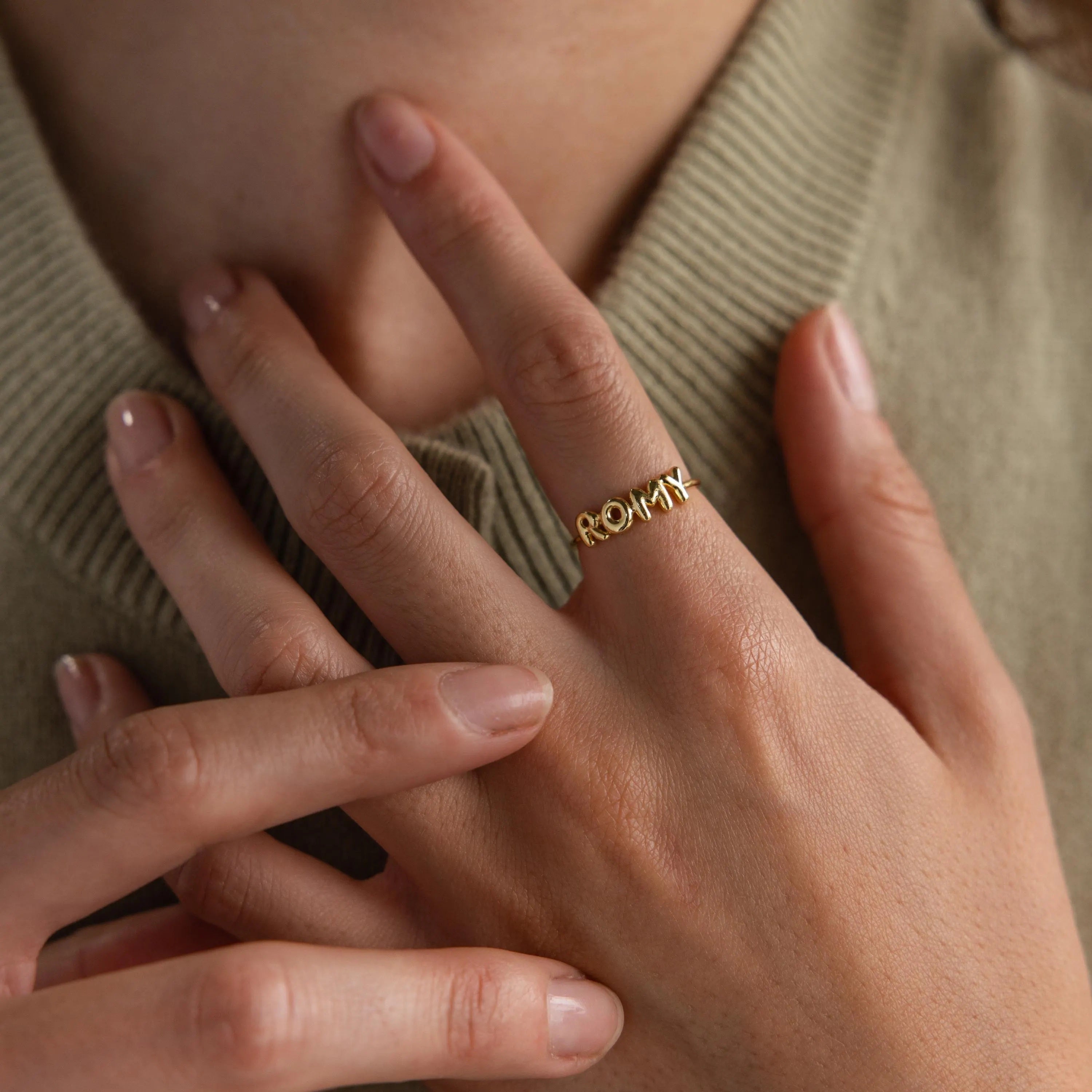 Model wearing a dainty gold bubble letter ring with the name "ROMY".