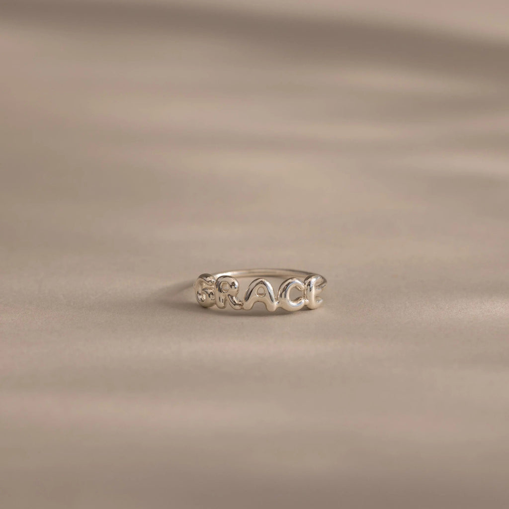 Close up of a dainty silver bubble letter ring with the name "GRACE".