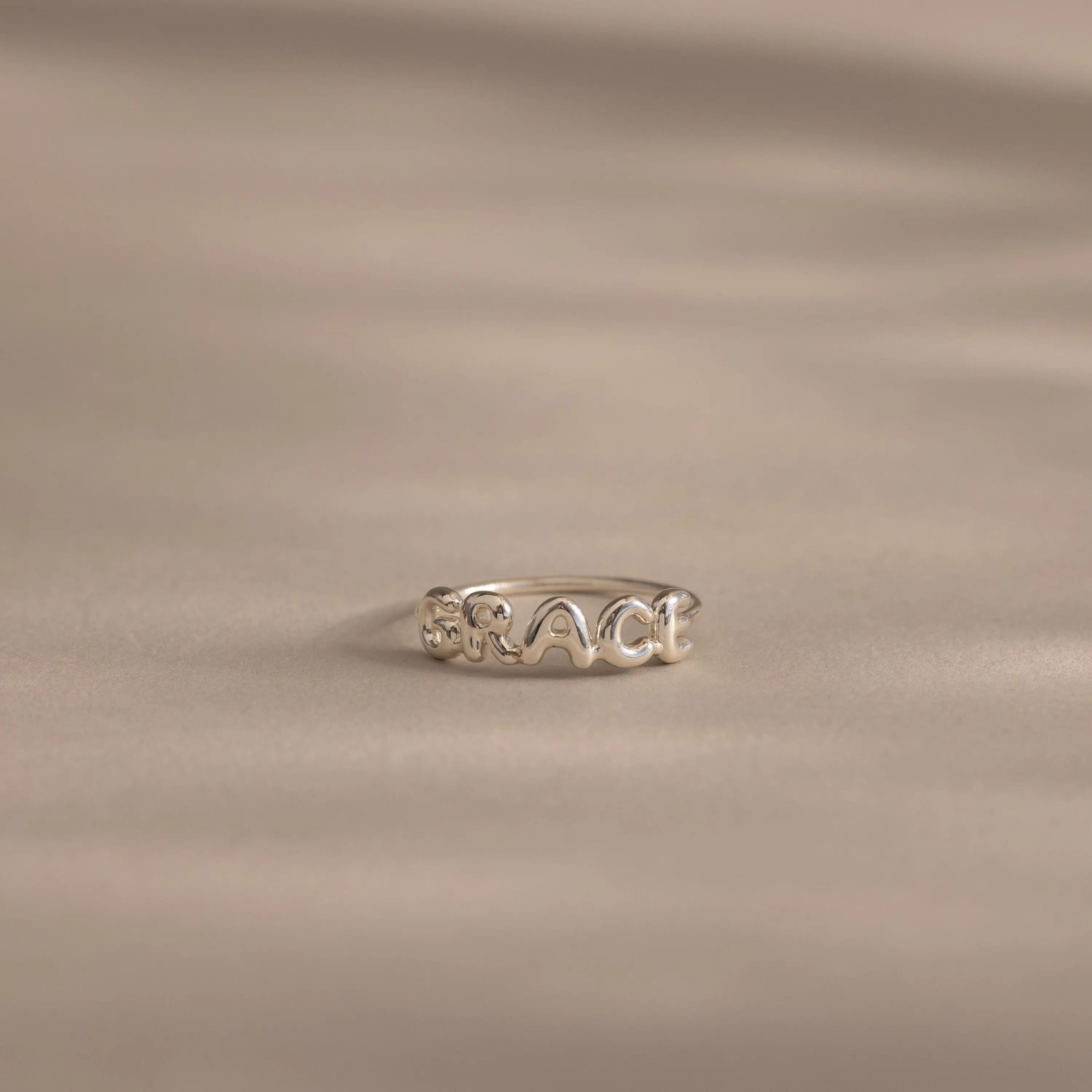 Close up of a dainty silver bubble letter ring with the name "GRACE".