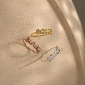 Three Bubble Name Rings with 3D letters spelling ROMY, DJANI, and GRAN rest on a textured beige surface—each a unique personalized ring, ideal for mixing and stacking.