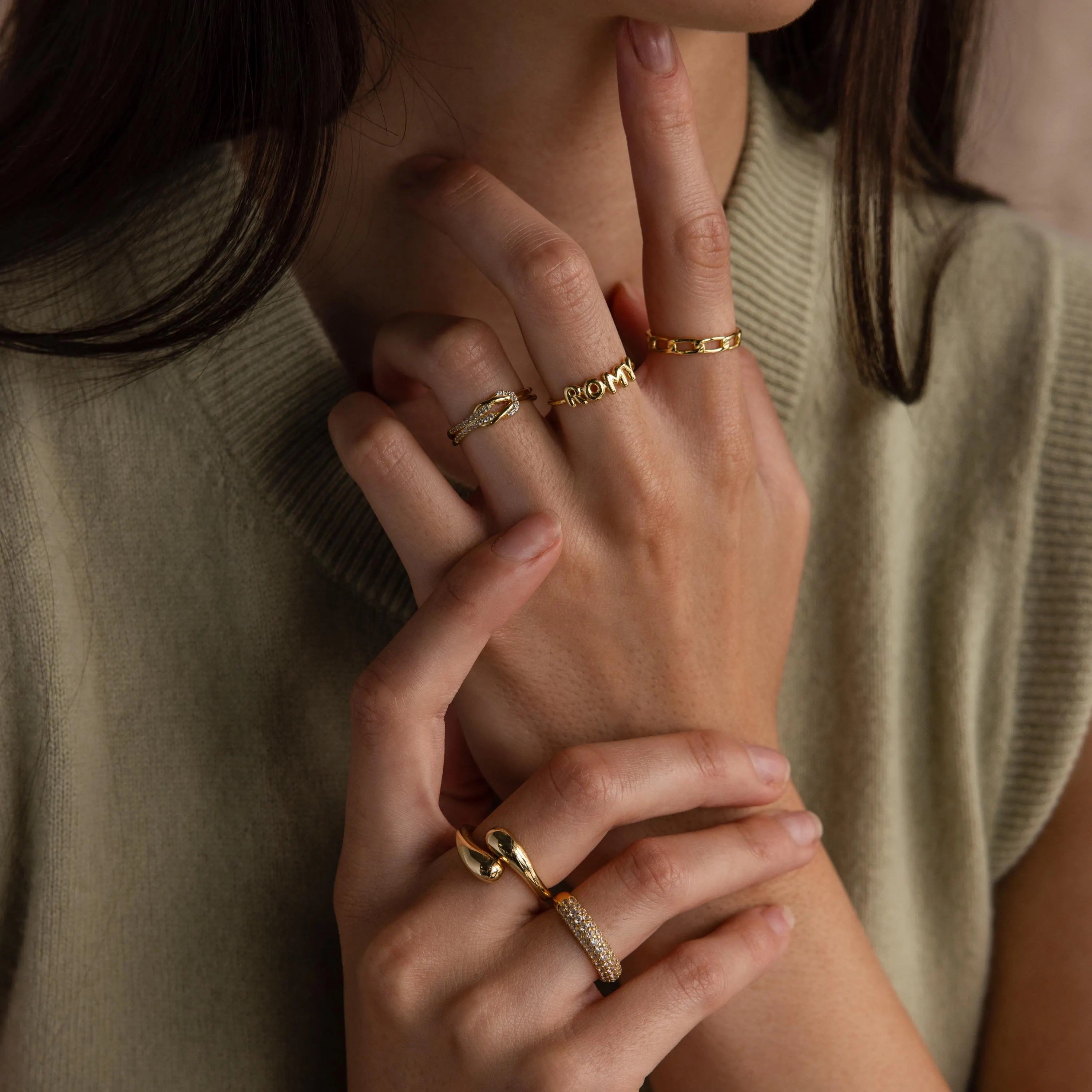 Up close of model wearing a gold bubble letter ring with the name "ROMY" styled with multiple matching gold stacking and statement rings.