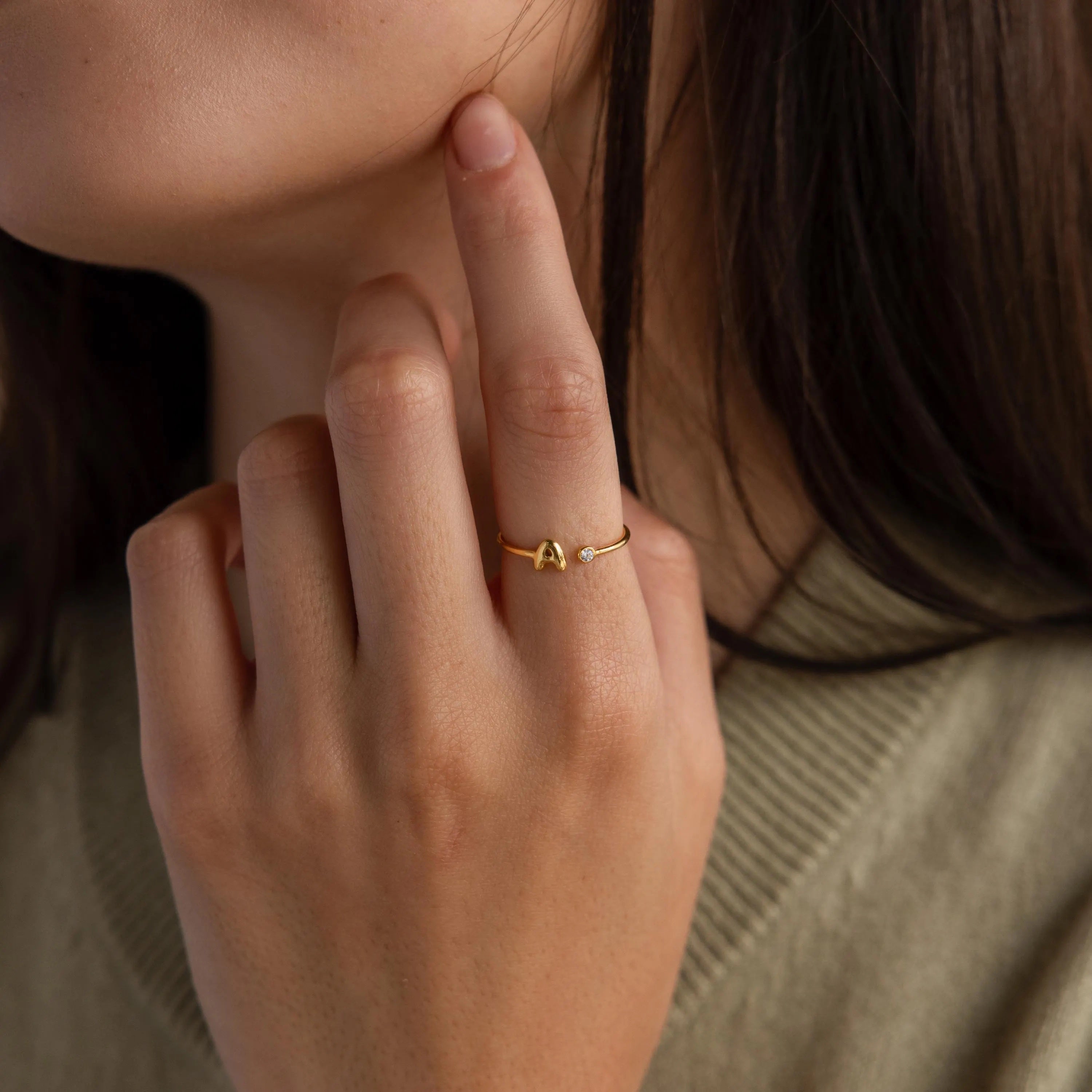 Up close of model wearing a dainty gold bubble letter birthstone duo ring with the initial "A" and a clear diamond gemstone.