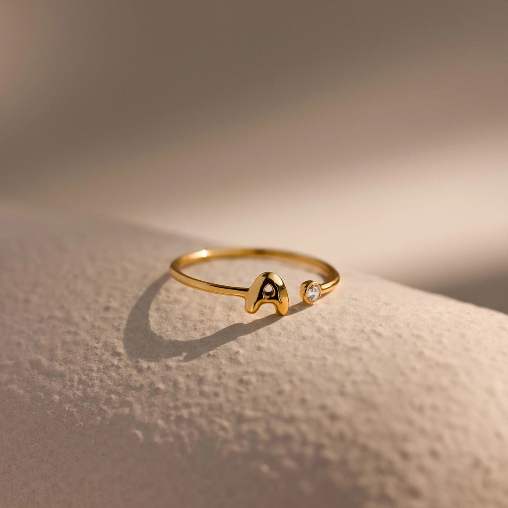 Up close of a dainty gold bubble letter gemstone duo ring with the initial "A" and a clear diamond birthstone.