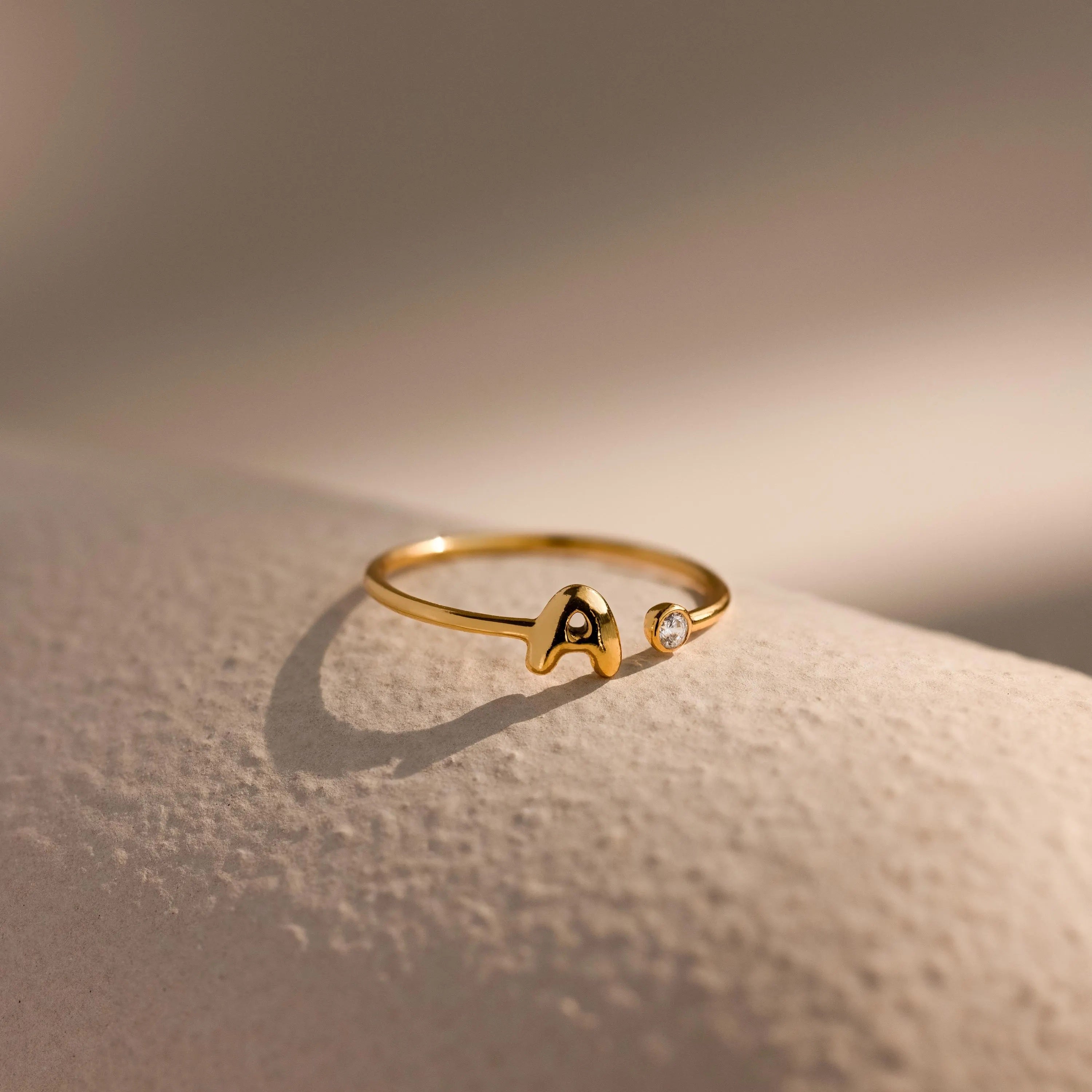 Up close of a dainty gold bubble letter gemstone duo ring with the initial "A" and a clear diamond birthstone.