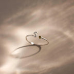 Up close of a silver bubble letter duo gemstone ring with the initial "S" and a green peridot birthstone displayed on a neutral surface.