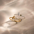 Up close of 2 bubble initial duo gemstone rings, featuring a gold ring with the letter "A" and a clear diamond birthstone and a silver ring with the letter "S" and a green peridot birthstone.