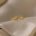 Close-up of a gold open ring featuring bubble-style initials K and J on soft satin fabric.