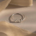 Close-up of a silver personalized ring with bubble letters H and G, styled on neutral beige fabric.