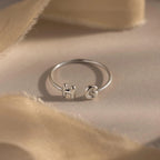 Close-up of a silver personalized ring with bubble letters H and G, styled on neutral beige fabric.