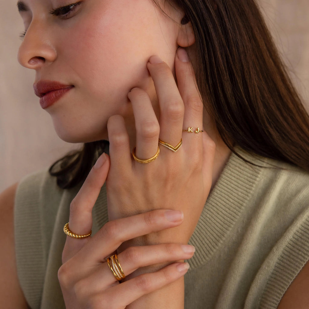 Close-up of a model showcasing layered gold rings, including a personalized KJ initial ring, V-band ring, rope band, and twisted stacking rings.