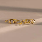 Set of custom gold initial rings with rounded puffy letters, spelling E, B, K, J, R, and C, arranged side by side on a neutral surface.